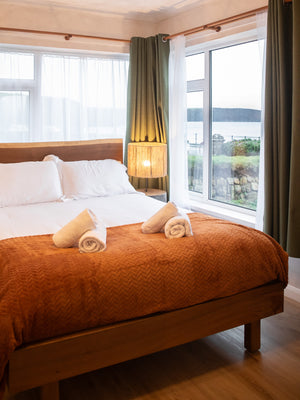 Coastal-styled room, with white linen and wooden furniture, wide windows showing Broad Haven sea view.