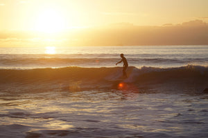 Surfer catching a wave at Broad Haven Beach during sunset.