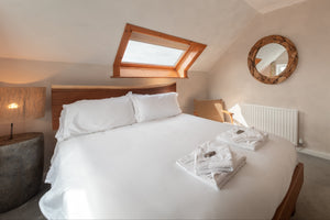 Coastal bedroom with white linen, driftwood mirror, and window with a view of Broad Haven beach
